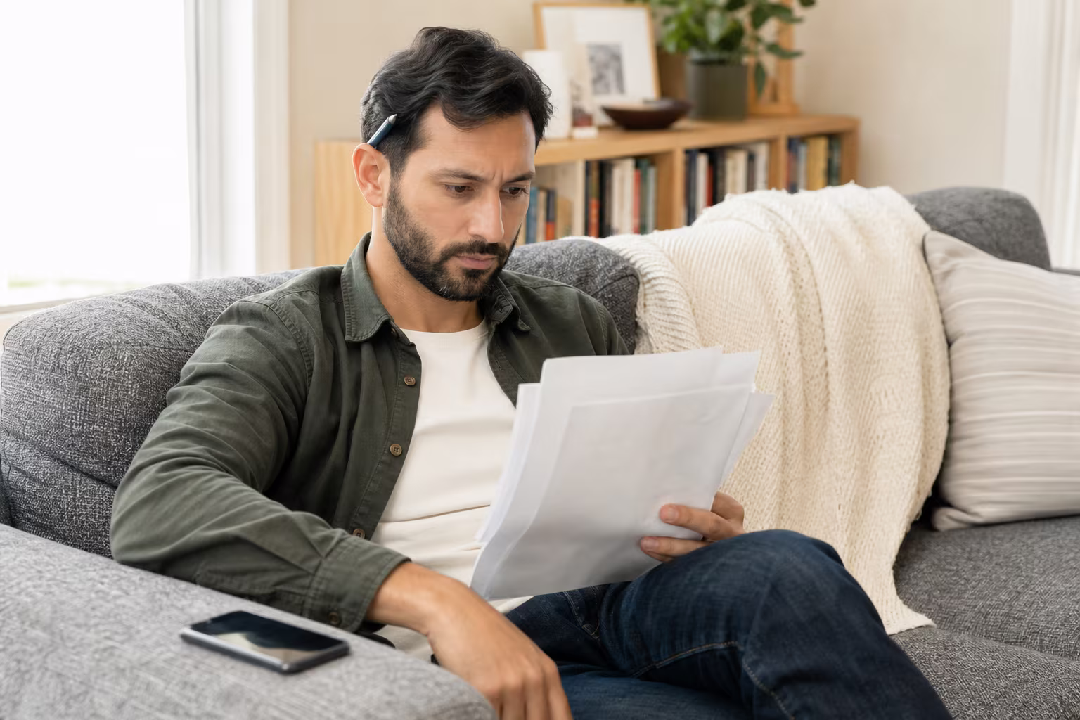 Someone sitting on a couch reviewing printed test results with a phone beside them